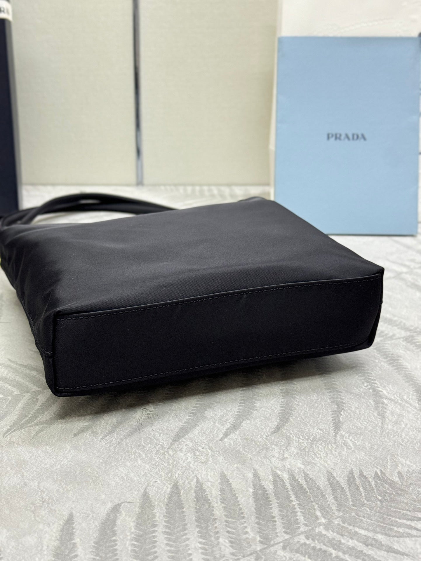 Black tote bag laid on side with structured base and top handles