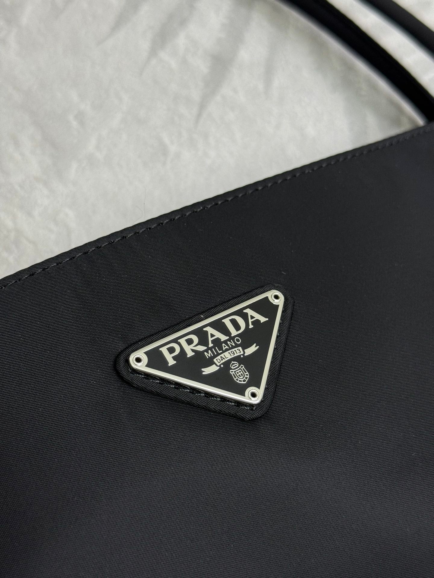 Black Prada tote bag front close-up of triangular PRADA logo plate.