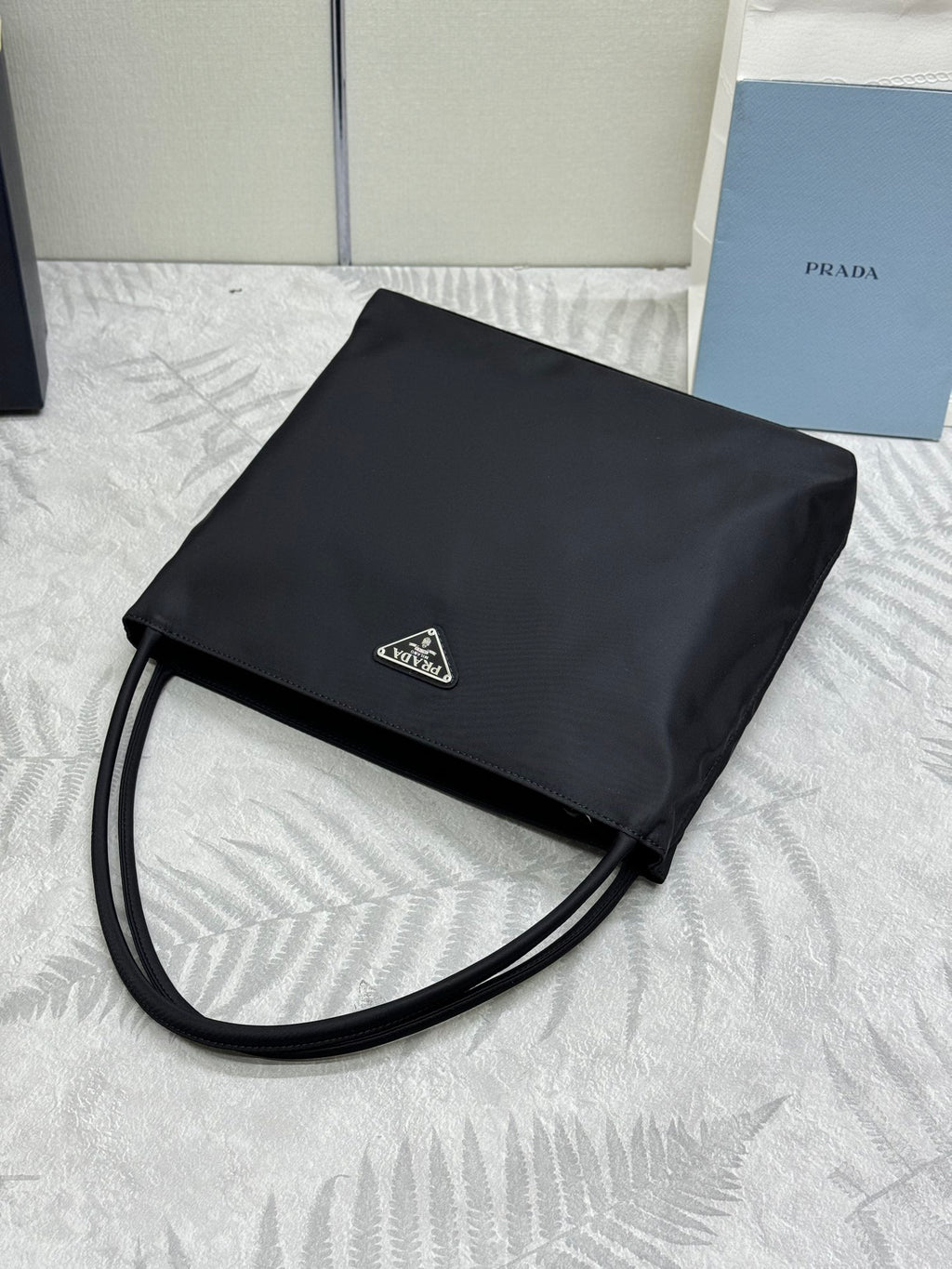 Black Prada small tote bag with long strap and foldover flap with logo plate.