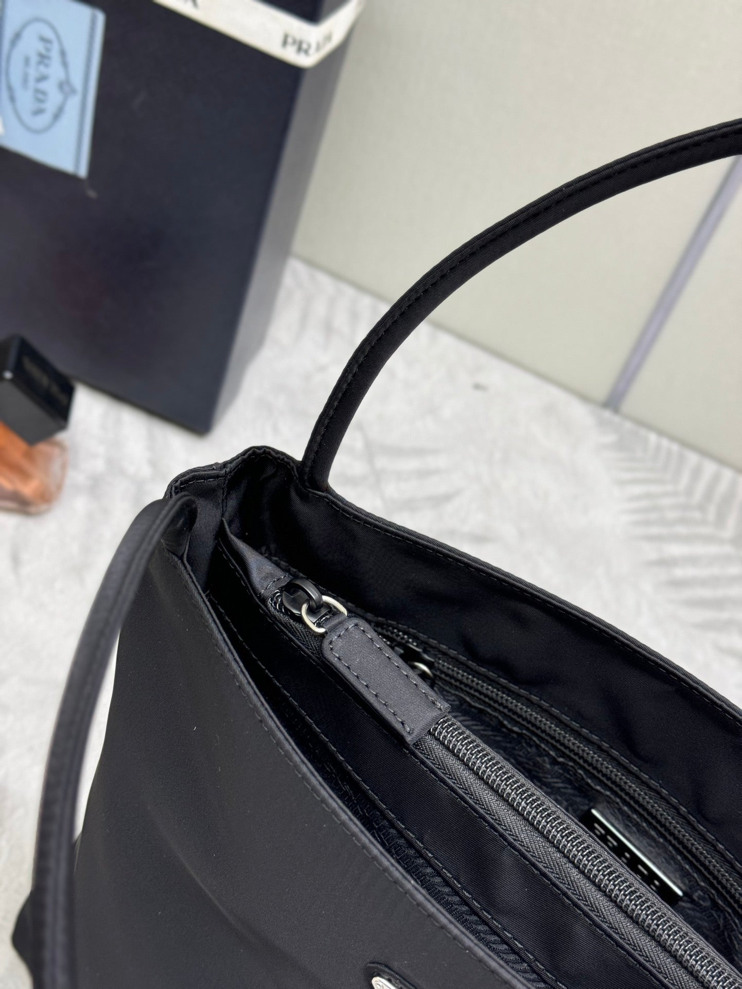 Black Prada tote bag top opening close-up with zip track and metal pull tabs.