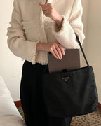Prada black tote bag with top handles and triangular logo plaque, held by person