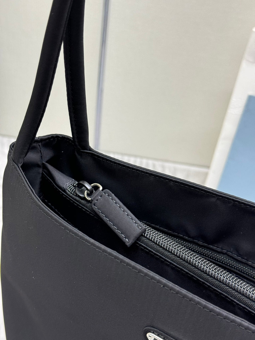 Prada tote bag close-up with zipper, stitched trim, and dark leather-look strap at top