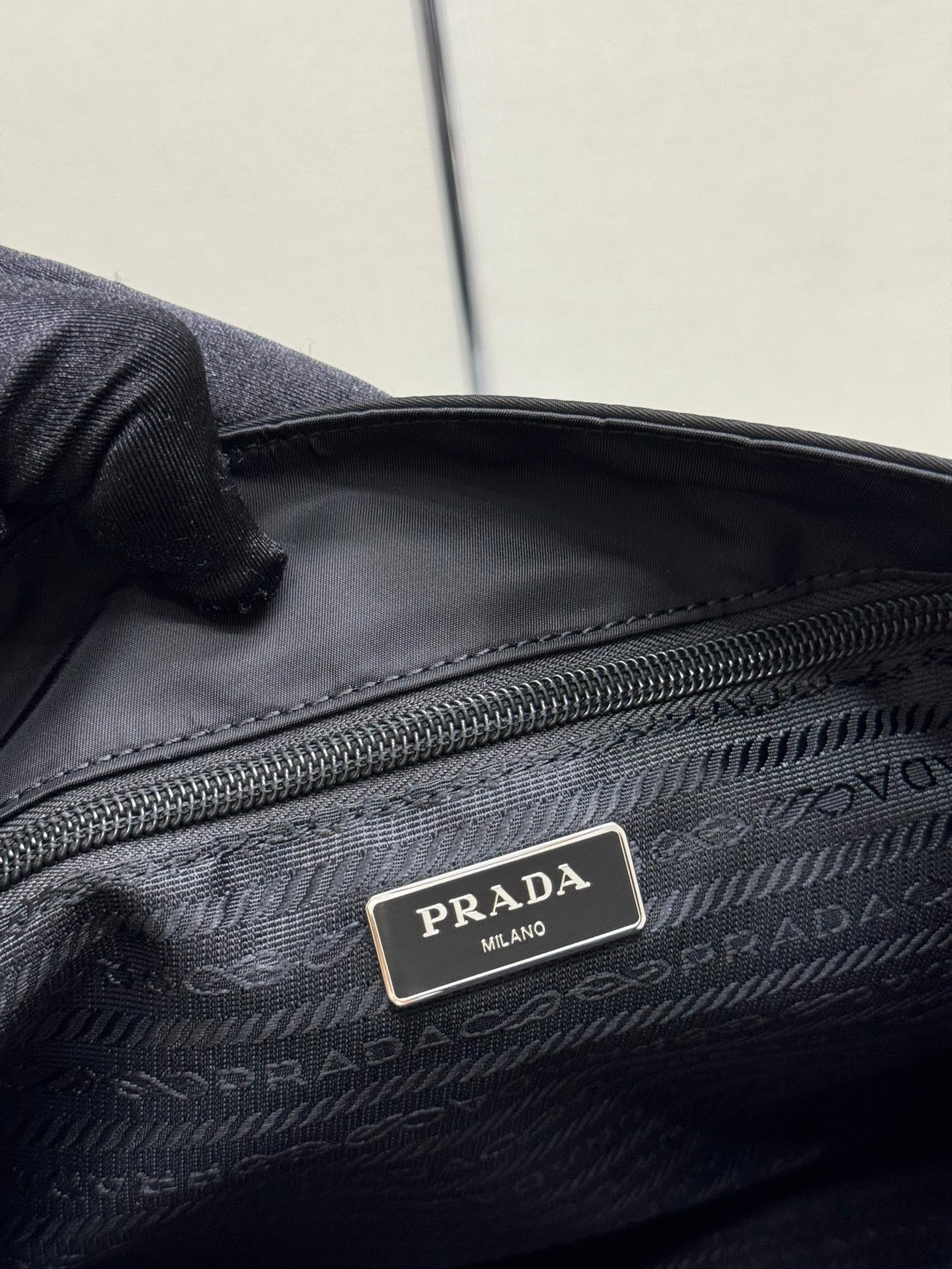 Prada interior logo plate on dark nylon lining near zipper and woven fabric texture