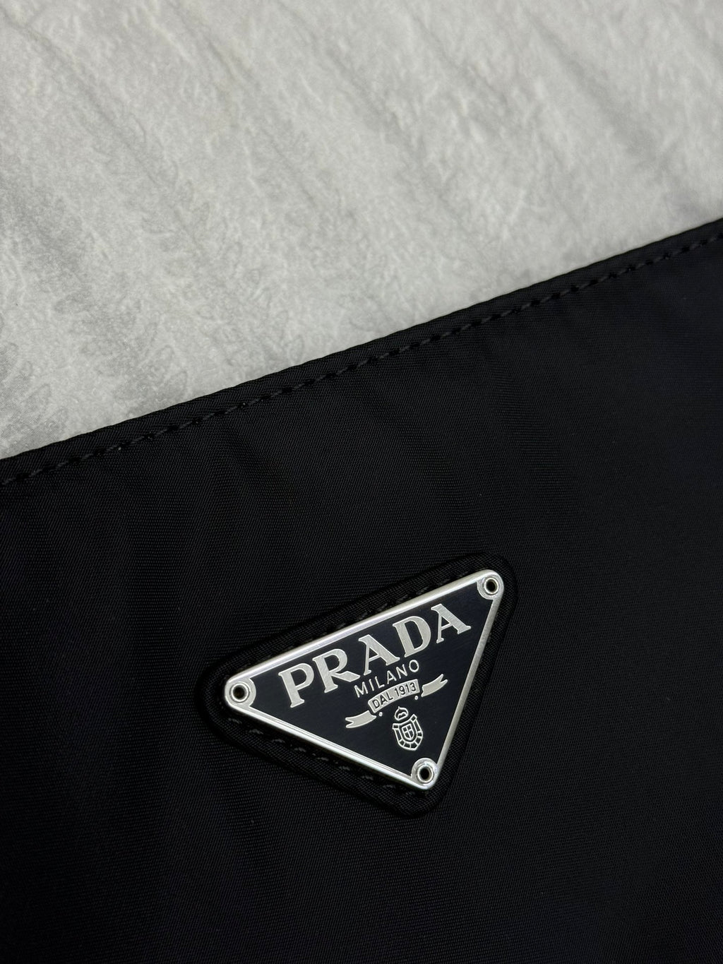 Prada logo patch on dark nylon fabric with metal triangle badge reading PRADA MILANO