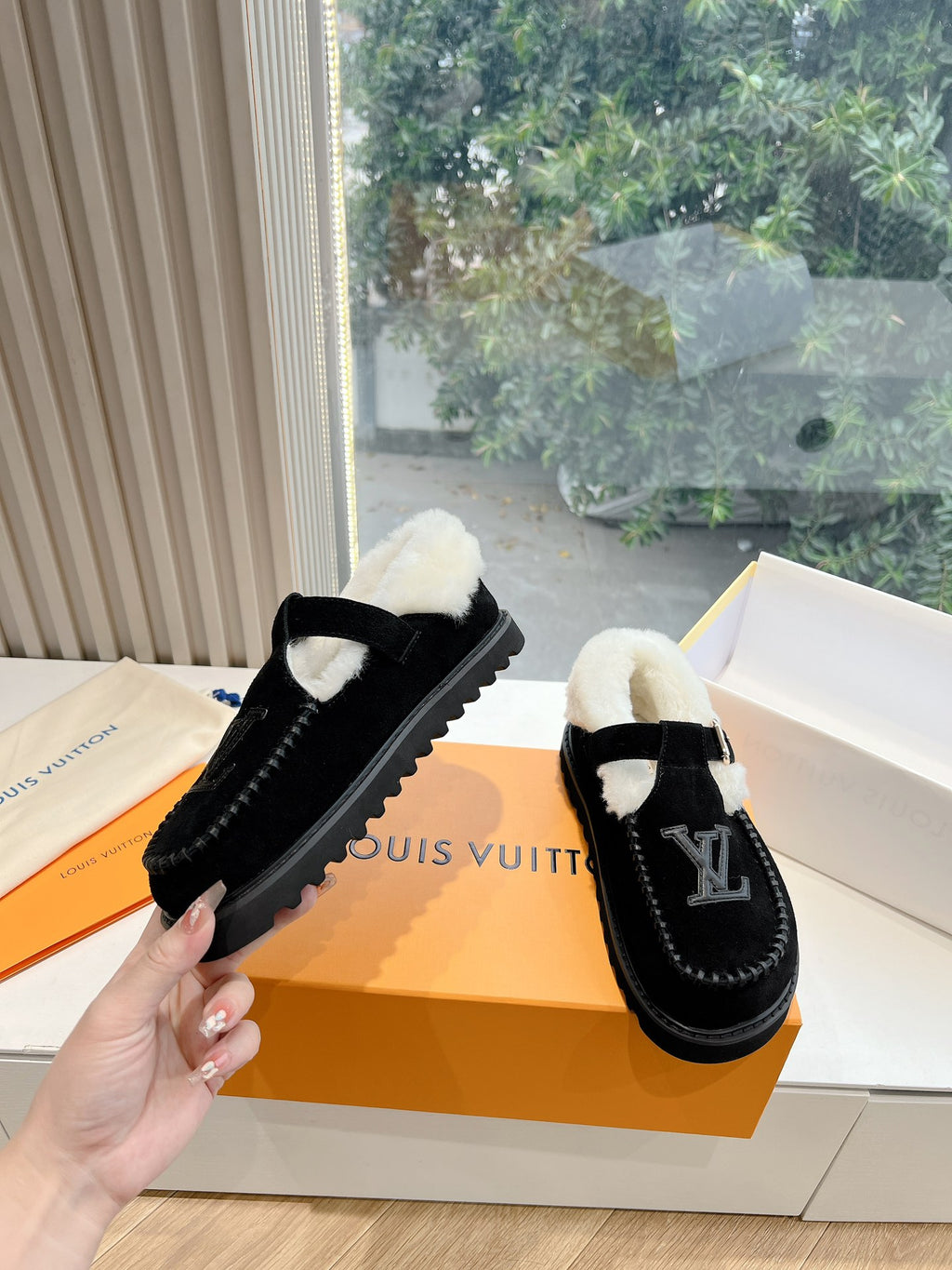 Hand holding black Louis Vuitton loafers with cream shearling collar and LV logo
