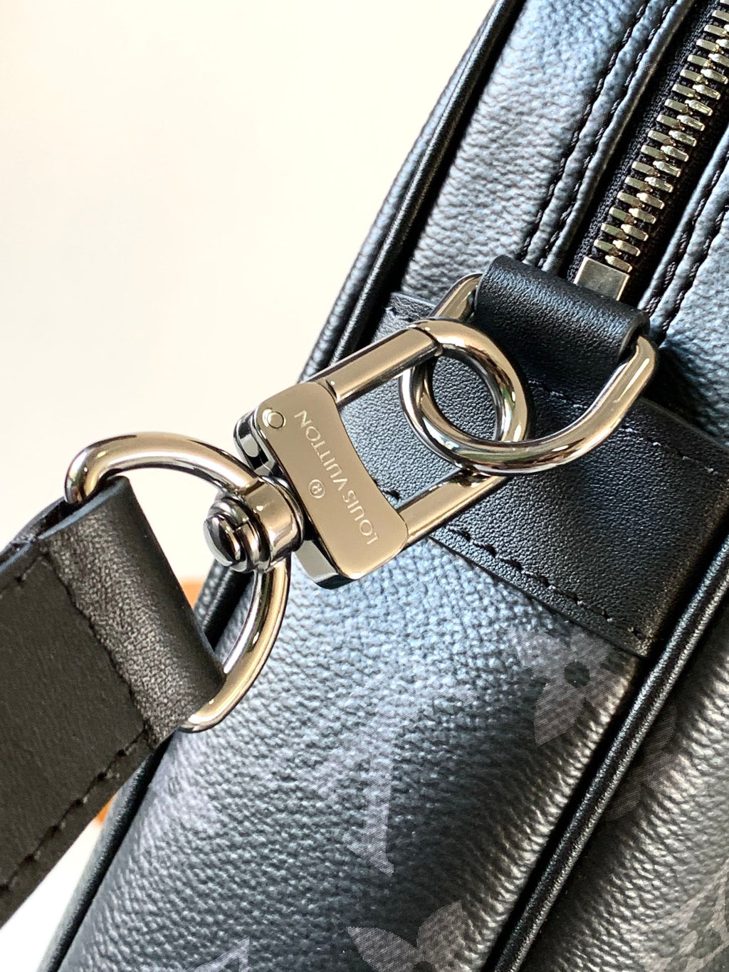 Handbag hardware close-up with gold-toned rings and clasp on dark monogram strap