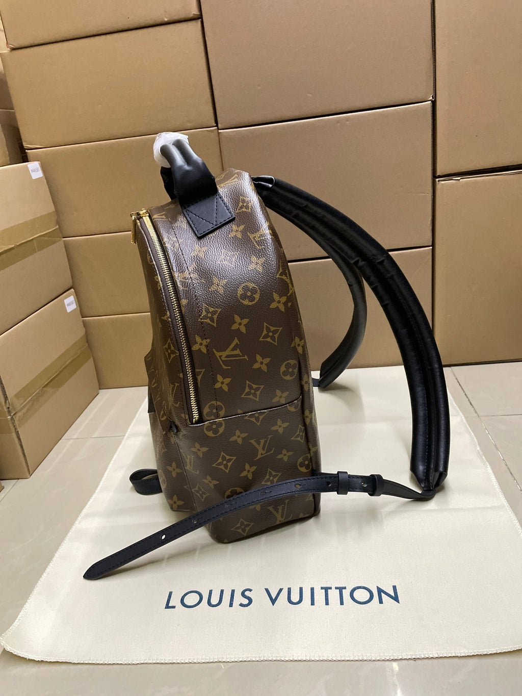 Monogram canvas backpack side view with black leather straps and hanging tag