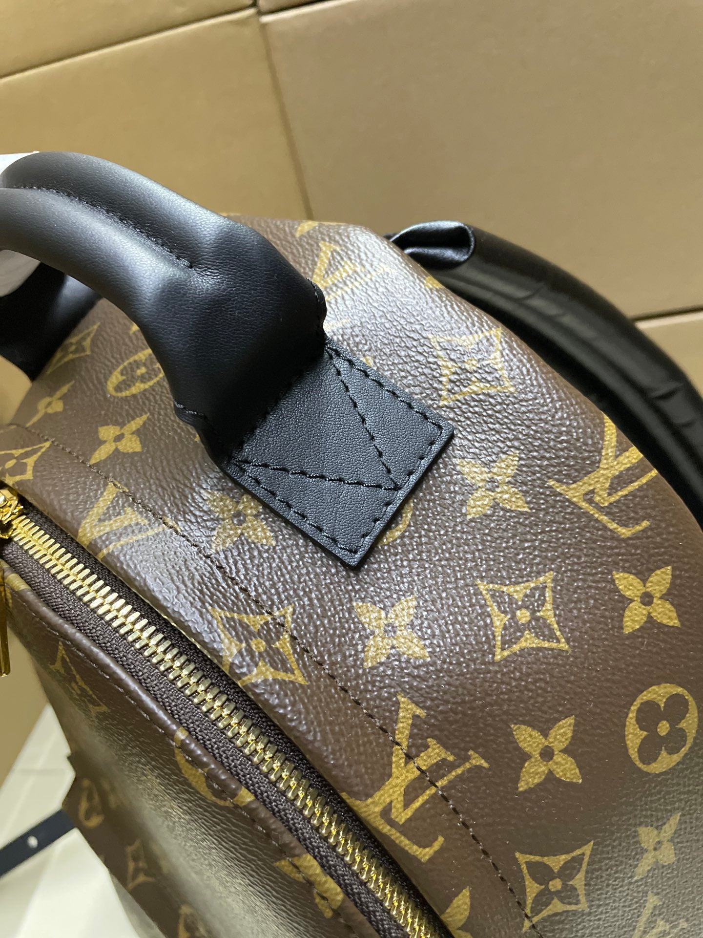 Monogram canvas backpack corner with black leather patch and gold zipper edge