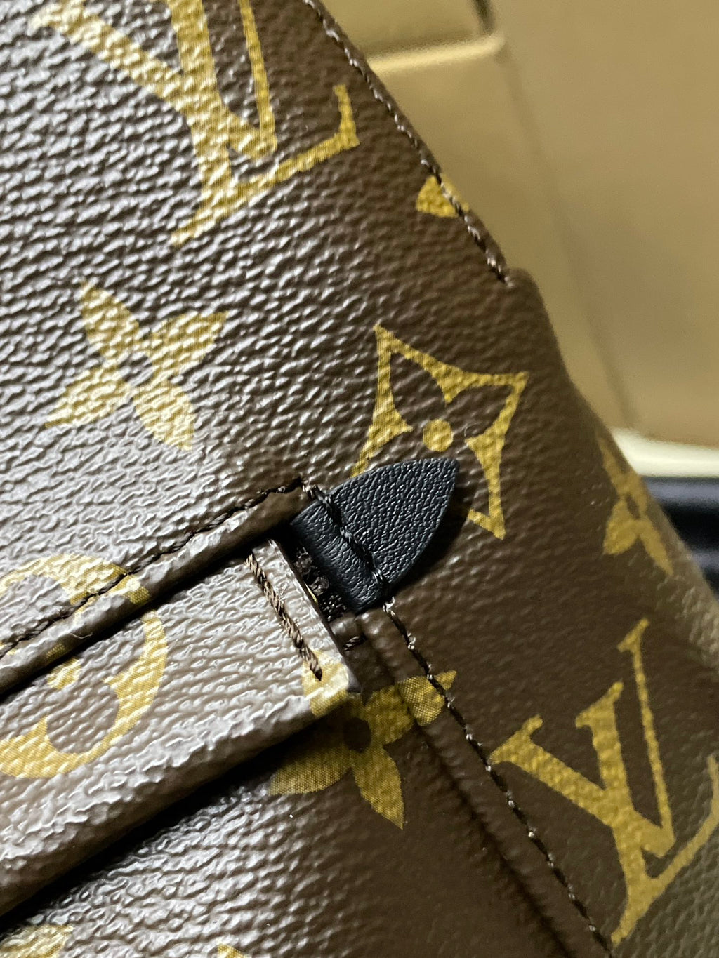 Monogram canvas backpack seam detail with black leather strap loop and stitching