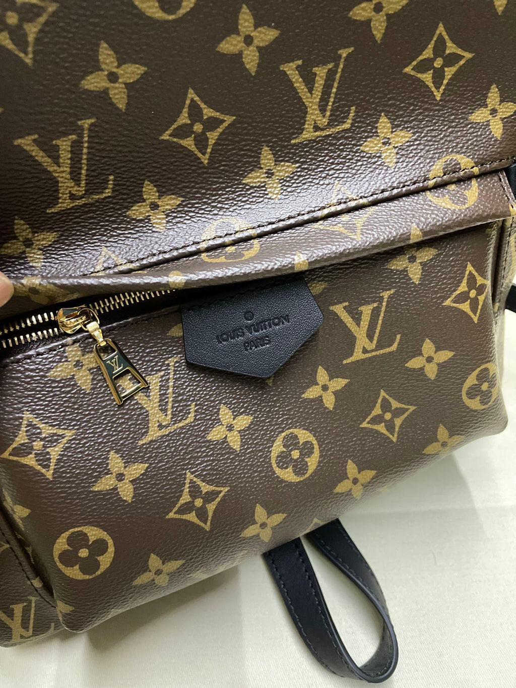 Monogram canvas pouch with gold zipper, leather zipper pull, and small tag detail
