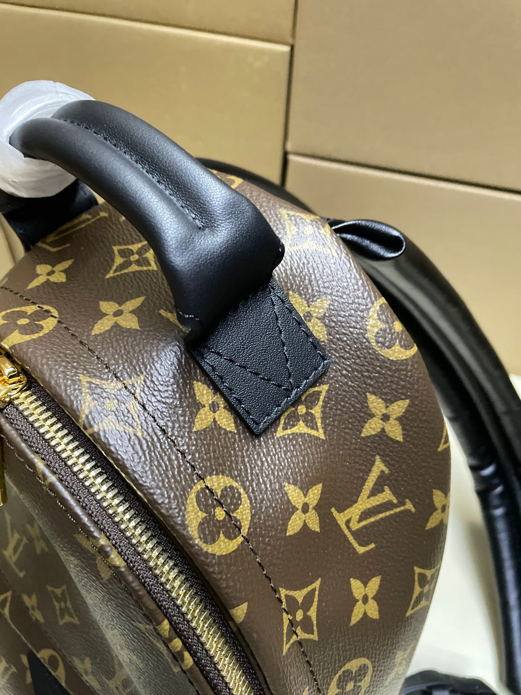 Monogram mini bag corner close-up with black leather tab and zipper on brown canvas