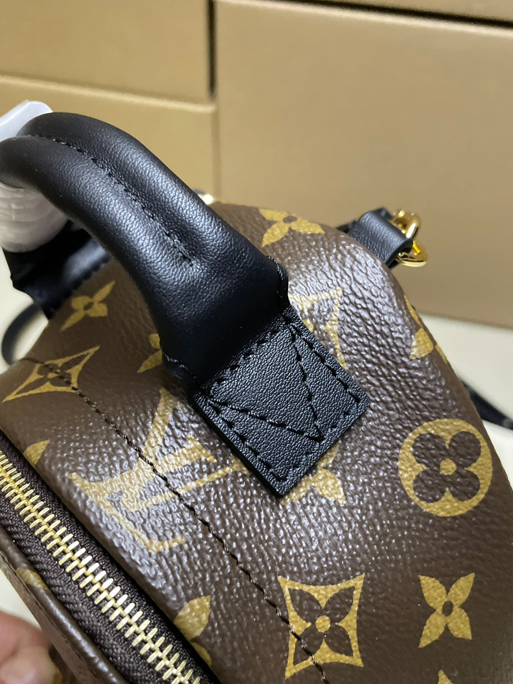 Monogram mini backpack bag close-up of leather strap tab and zipper pull