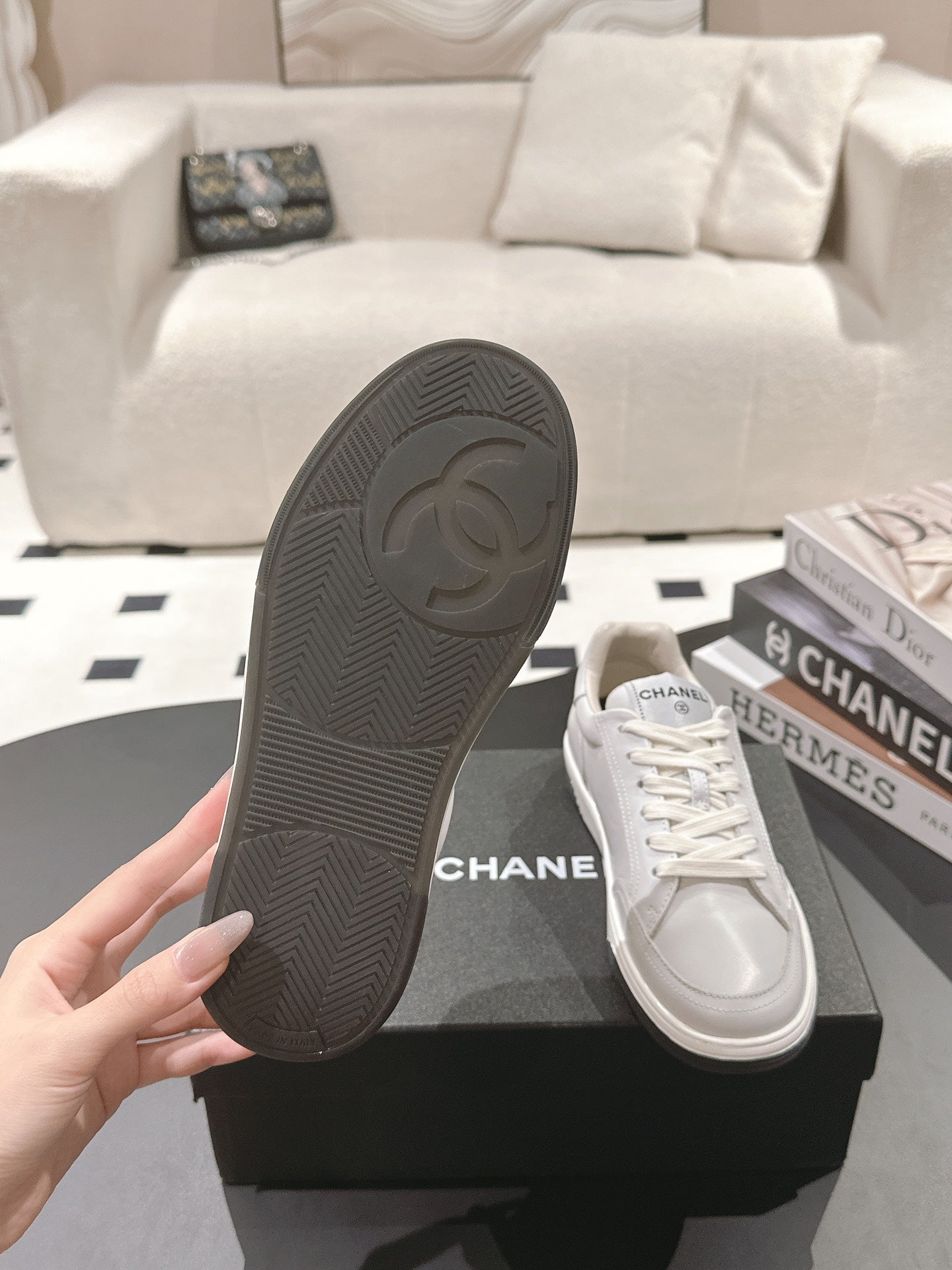 White leather sneaker with black rubber outsole, hand holding shoe bottom