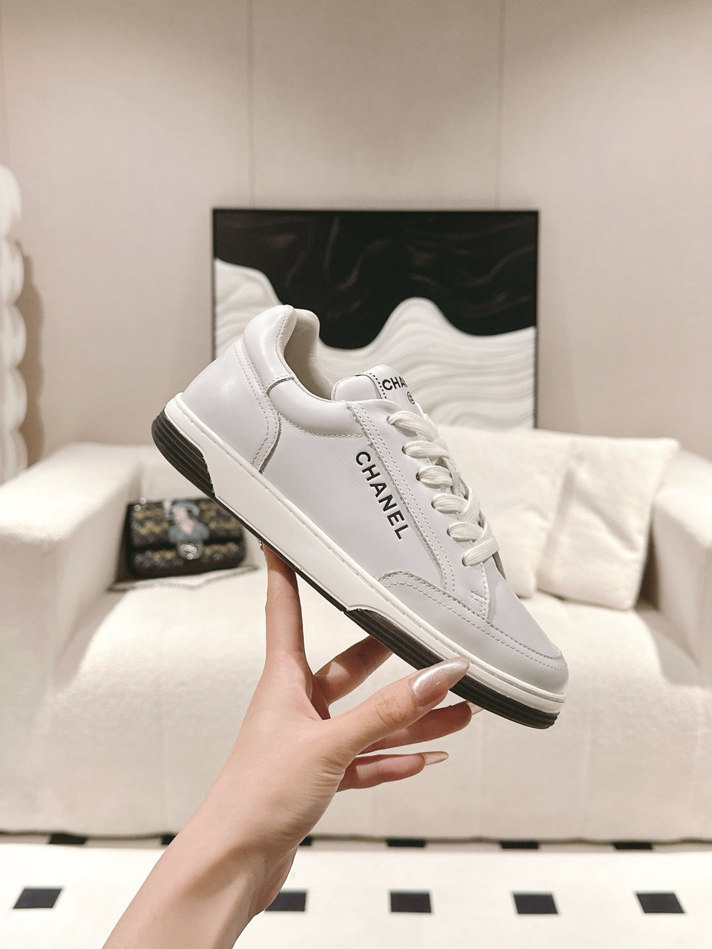 White leather low-top sneaker held upright, lace-up front with Chanel logo