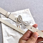 Cream leather belt with silver butterfly buckle and punched holes, close-up