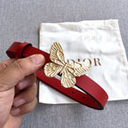 Red leather belt held in hand with gold-tone butterfly buckle and adjustment holes.