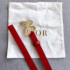 Red leather belt with gold-tone butterfly emblem and punched adjustment holes.