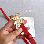 Gold-tone butterfly buckle on a red leather belt with punched adjustment holes.