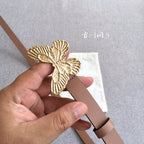 Dior belt detail view: gold butterfly buckle on brown strap held near the holes