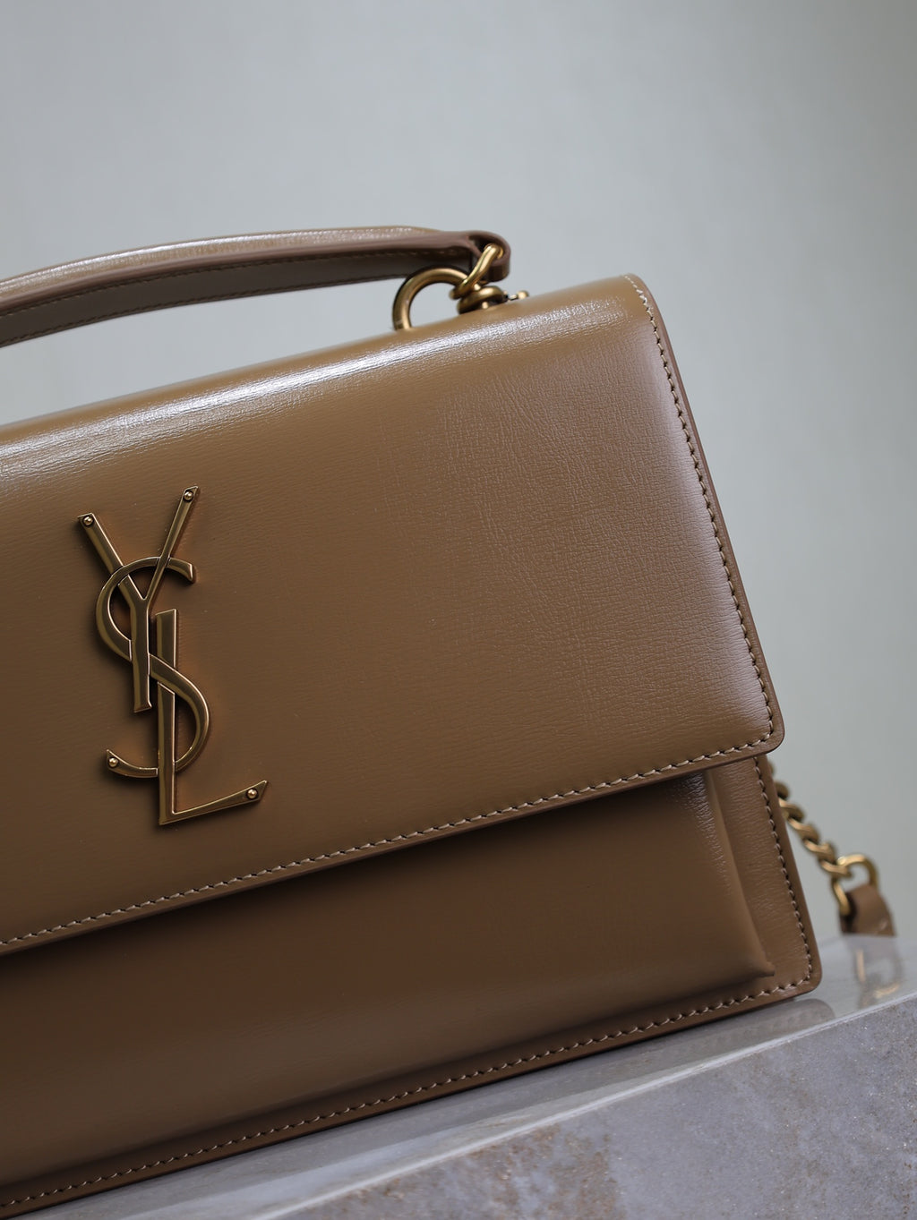 YSL tan flap bag detail with gold YSL logo and stitched front edge