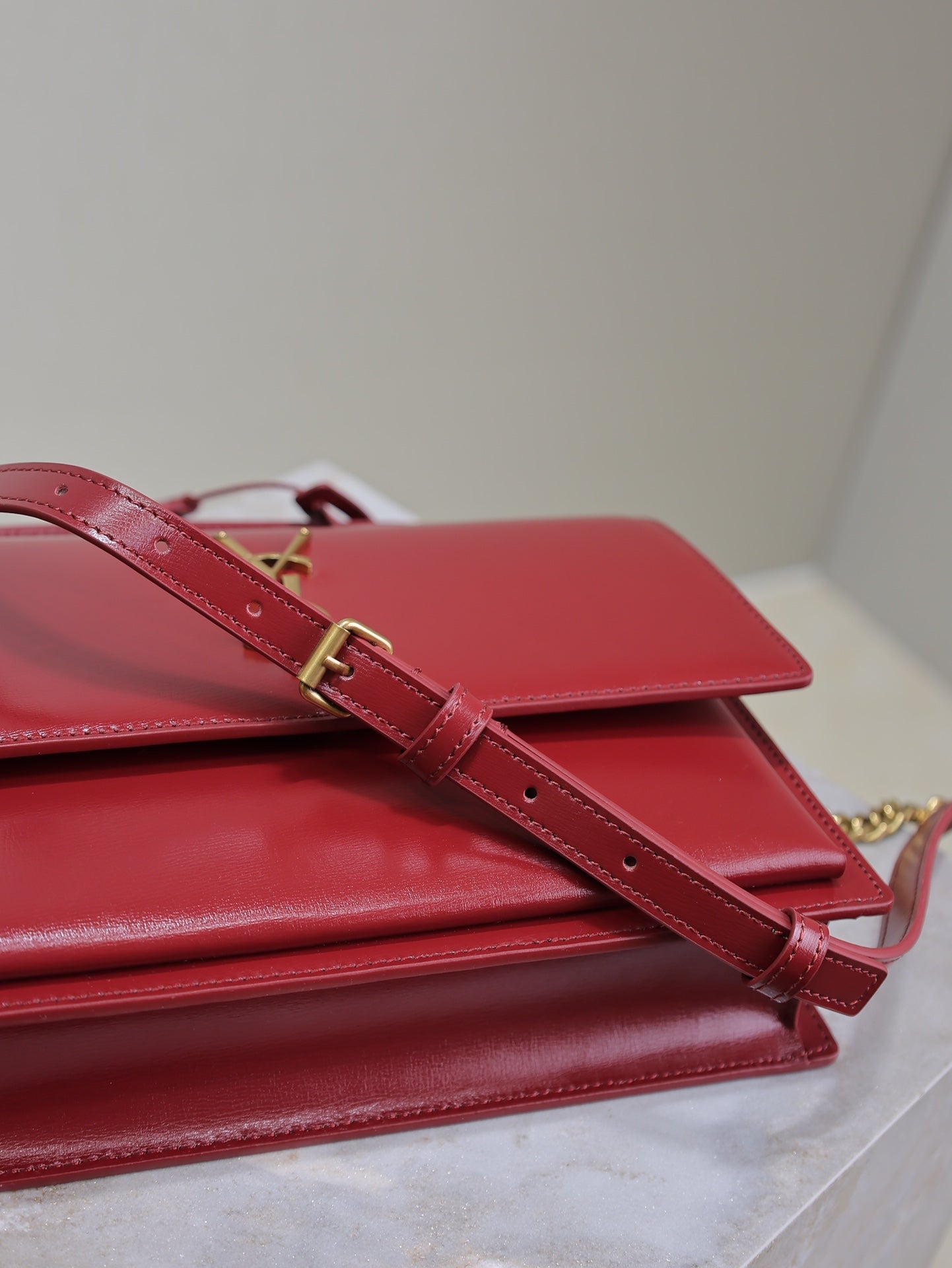 Red leather crossbody bag with adjustable strap and gold clasp, flap closed.