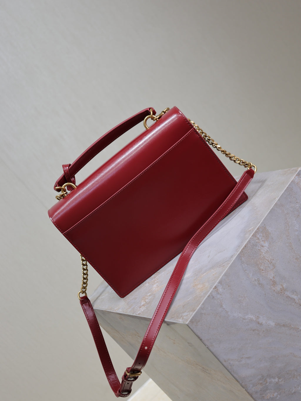 Red leather crossbody bag with chain strap and top handle, front flap closed.