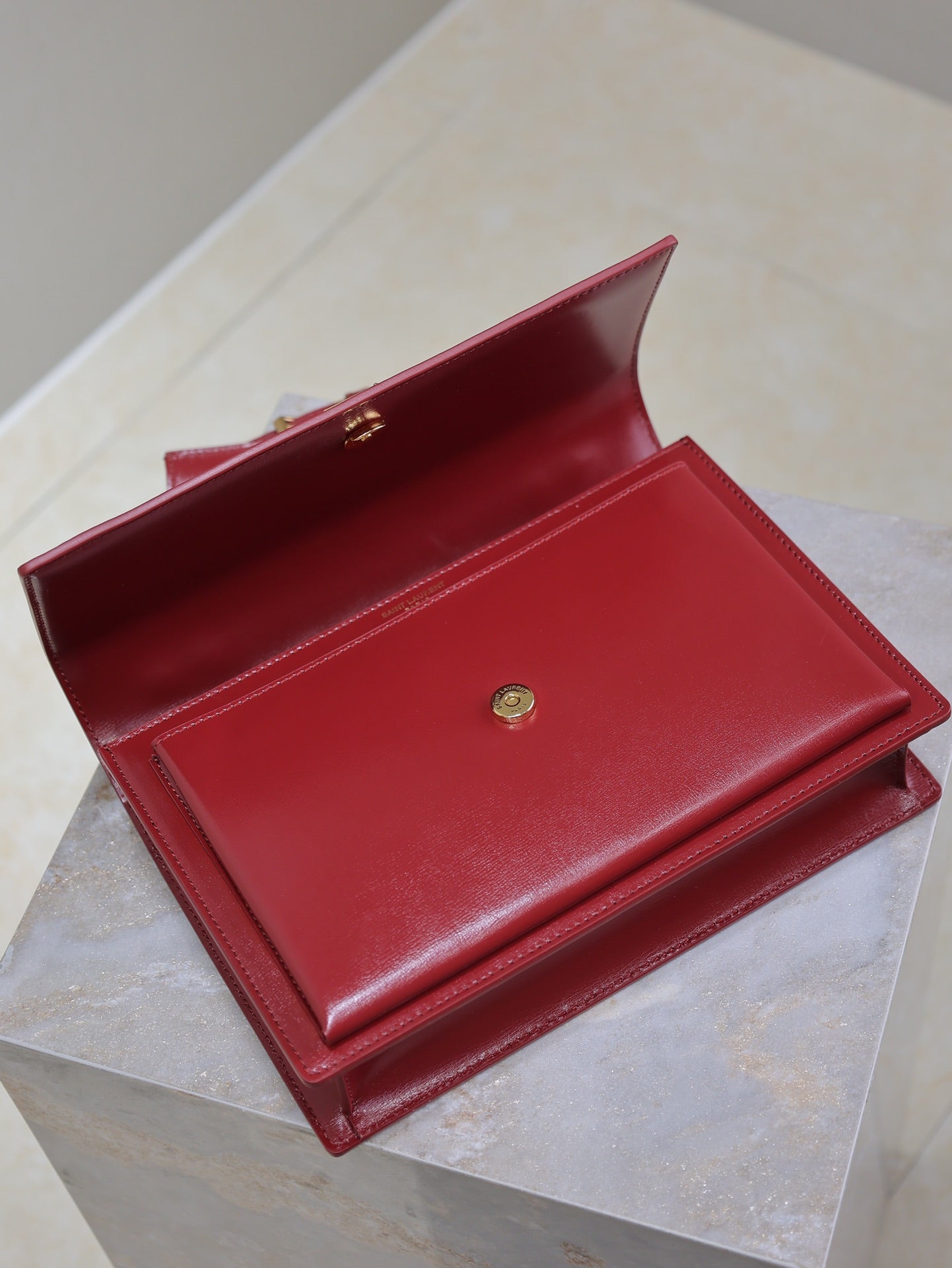 Red leather wallet-style bag with open flap and gold button closure.