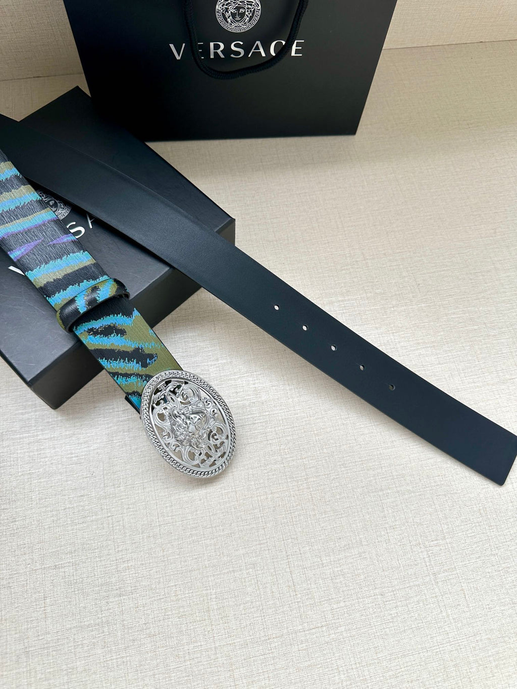 Versace belt laid flat: blue-green patterned strap with oval silver-tone buckle