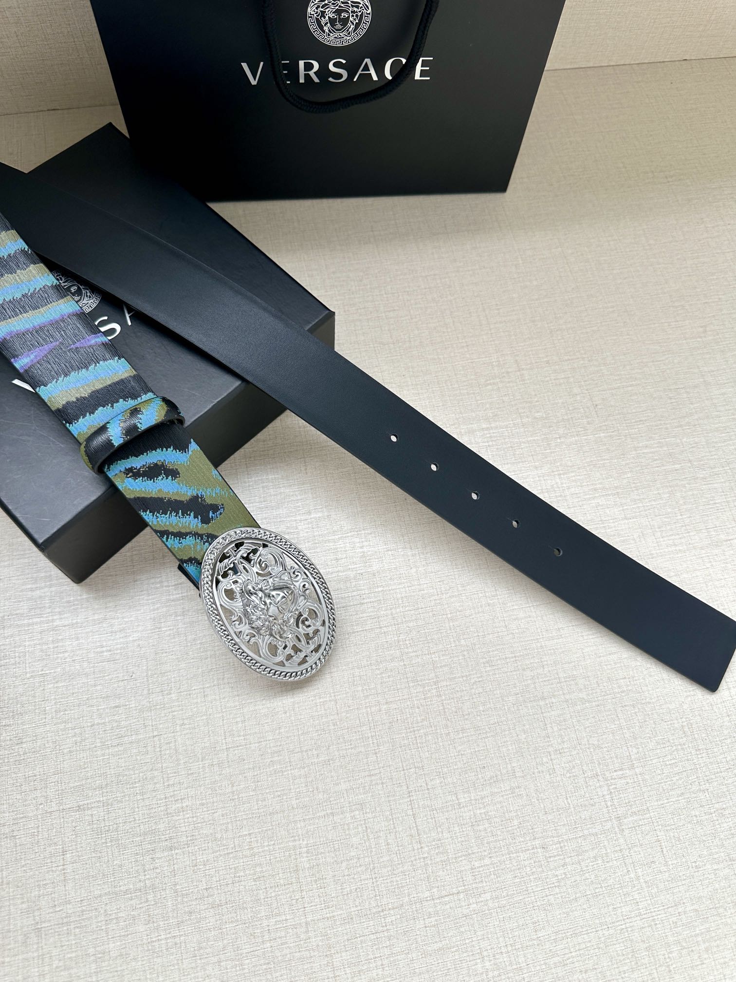 Versace belt laid flat: blue-green patterned strap with oval silver-tone buckle