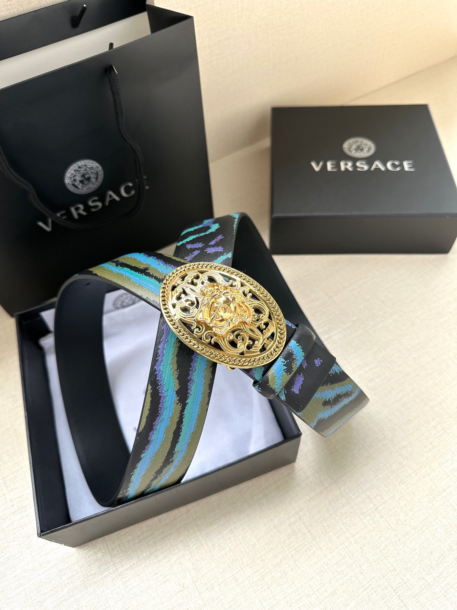 Versace belt with oval gold-tone buckle and blue-green patterned strap, shown in gift box