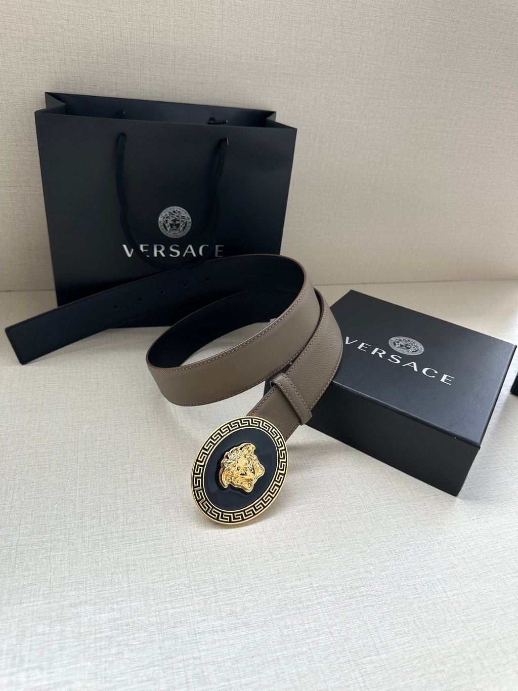 Leather belt laid flat with oval Medusa Medusa medallion buckle and gift box