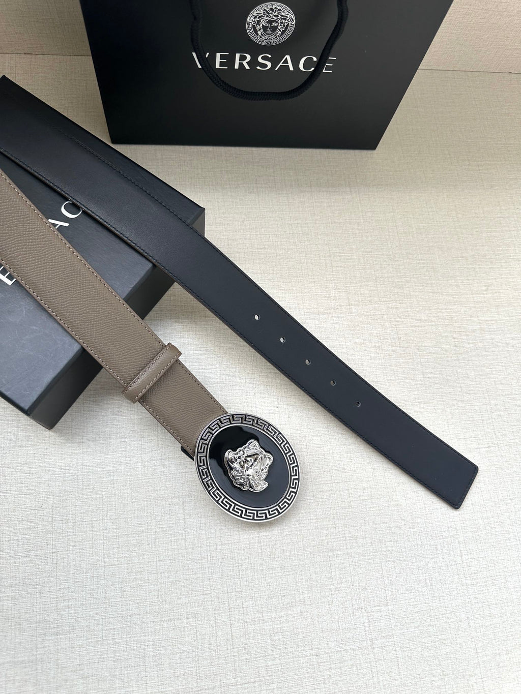 Leather belt with taupe strap and oval Greca Medusa buckle; holes along strap