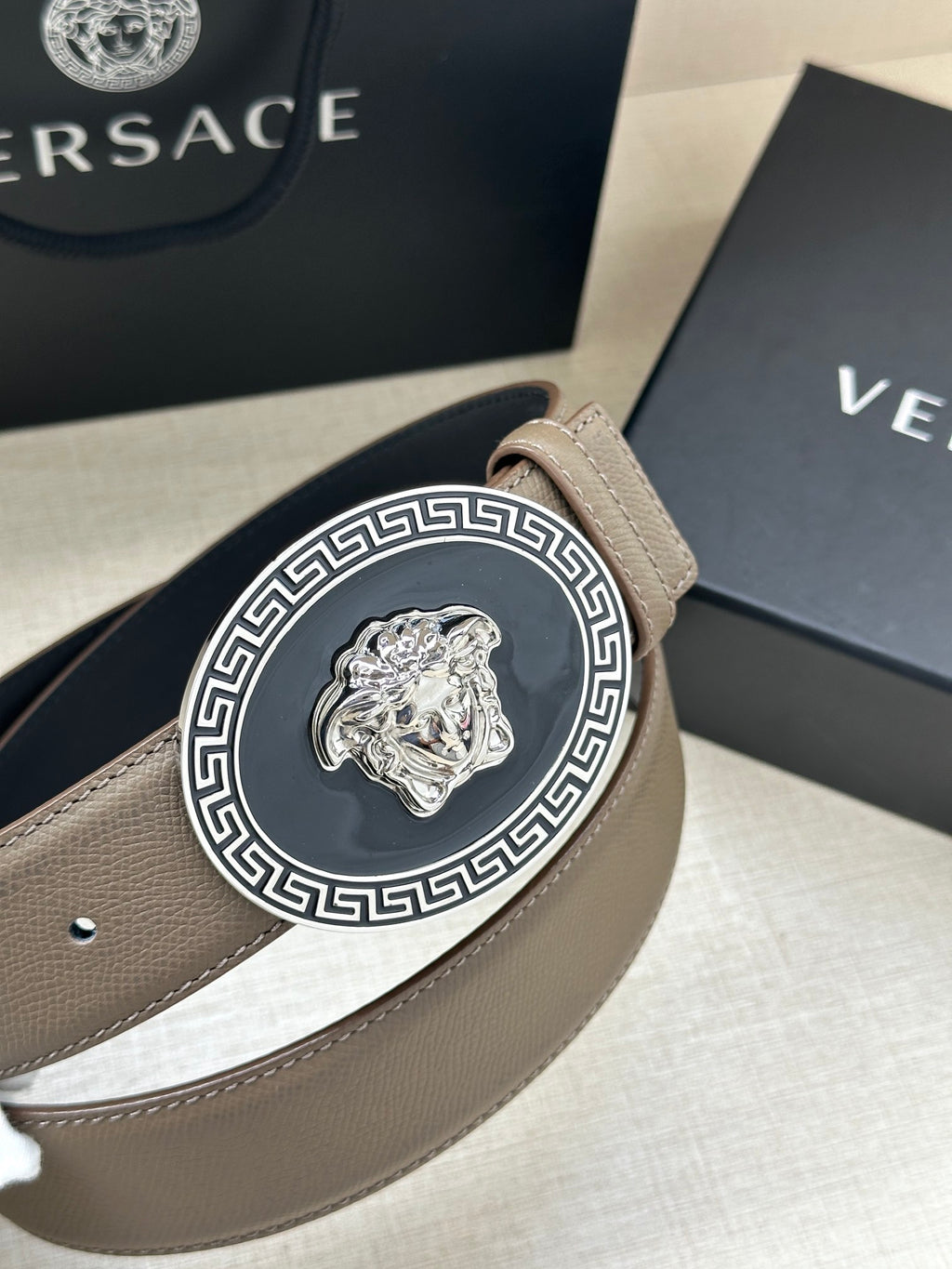 Leather belt close-up with light taupe strap and silver-tone Medusa Medallion