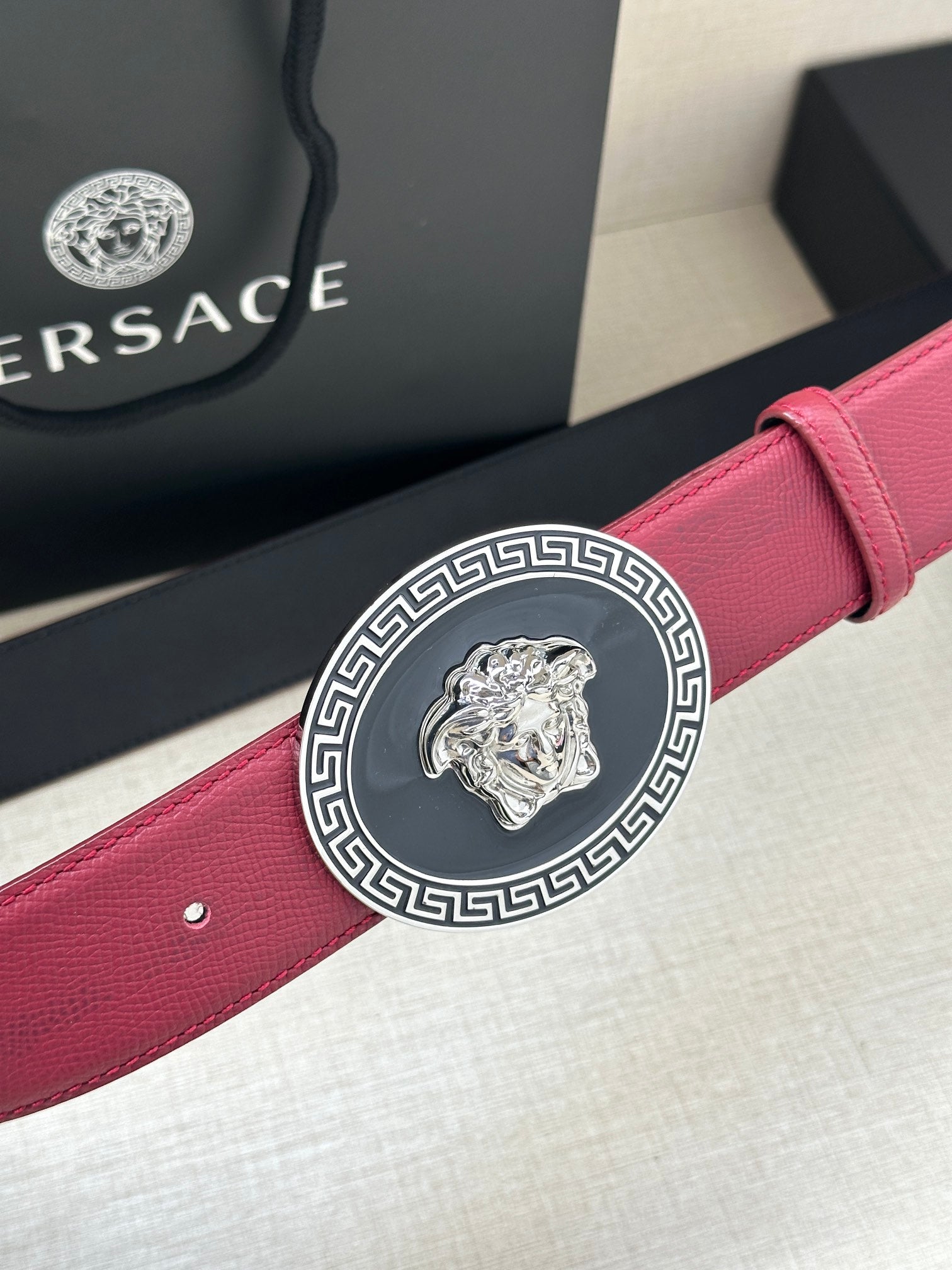 Maroon leather Versace belt viewed close-up with round gold Medusa buckle