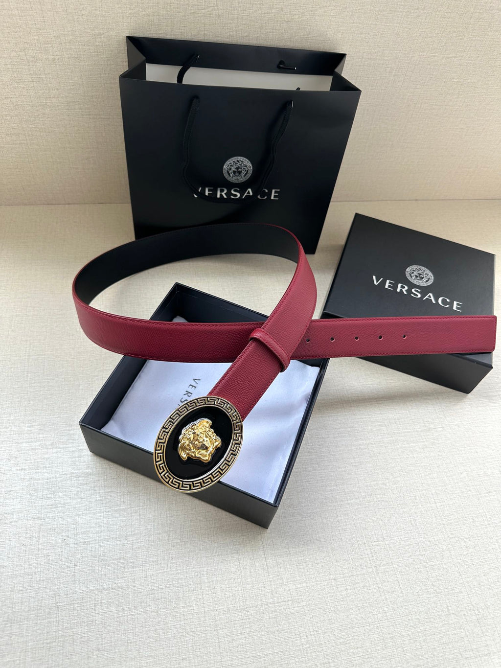 Versace maroon leather belt laid flat with circular gold Medusa buckle