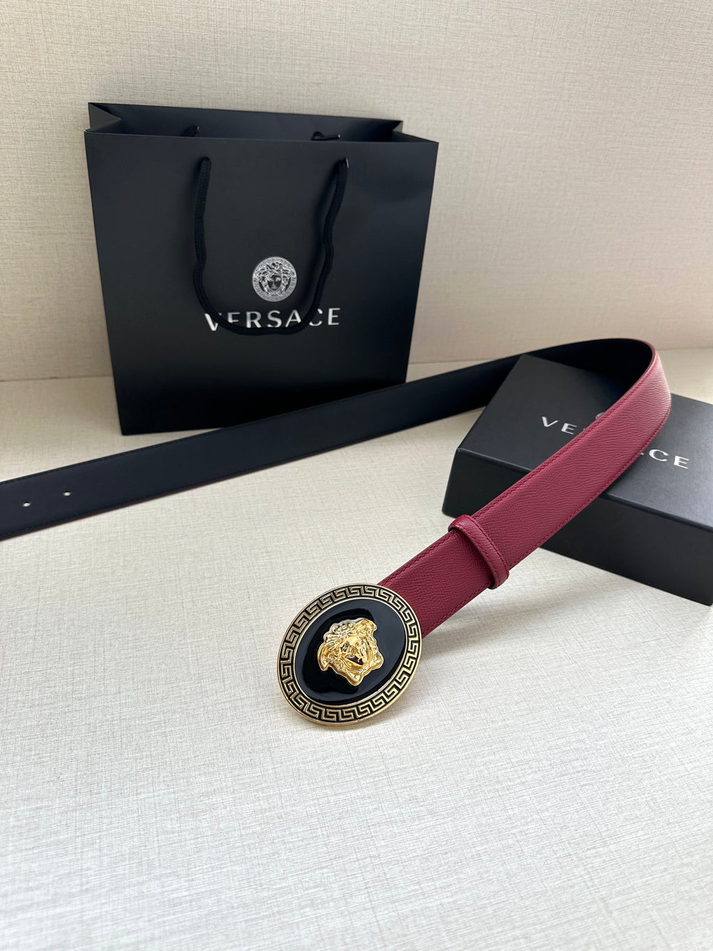 Versace maroon belt with round gold Medusa buckle and Greek key border, angled view