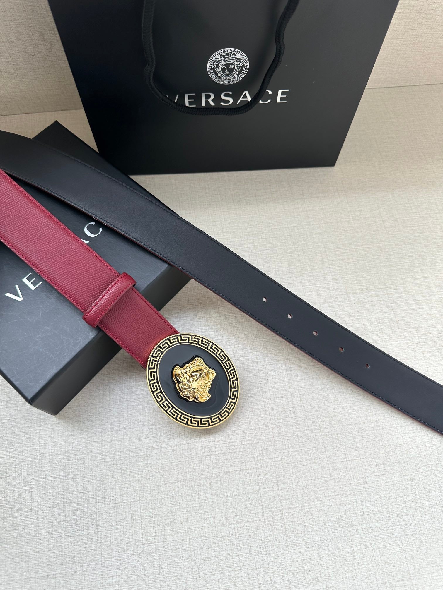 Close-up of maroon Versace belt strap with gold Greek key Medusa buckle