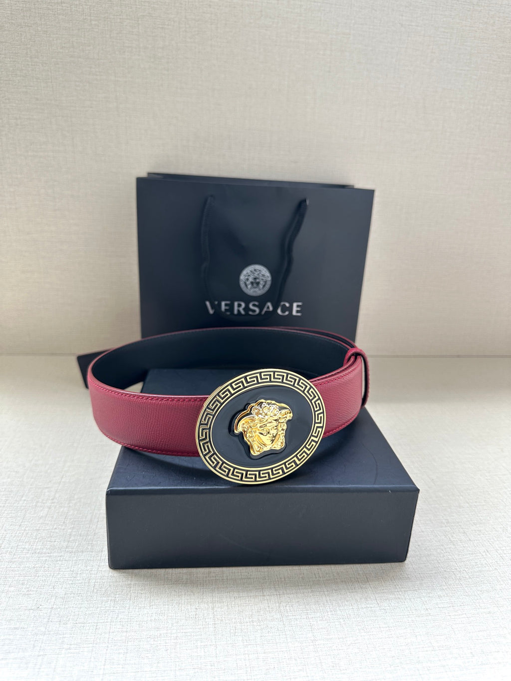 Versace belt in maroon leather with gold Medusa buckle on top of a gift box