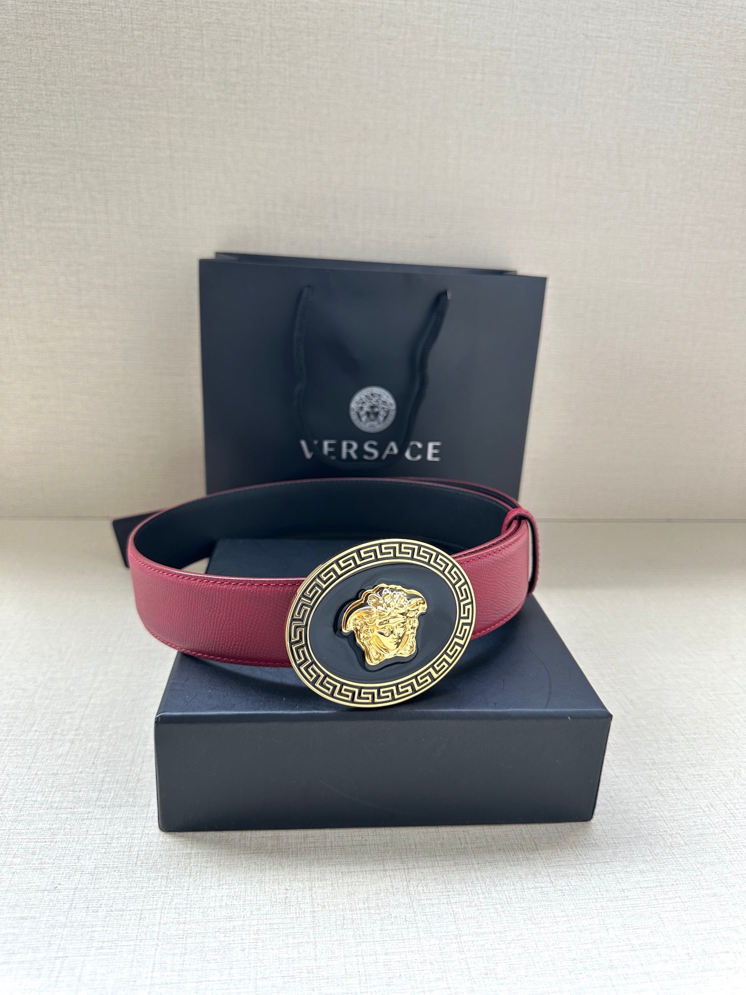 Versace belt in maroon leather with gold Medusa buckle on top of a gift box