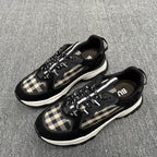 Pair of black sneakers with beige plaid panels, lace-up design, and white midsoles