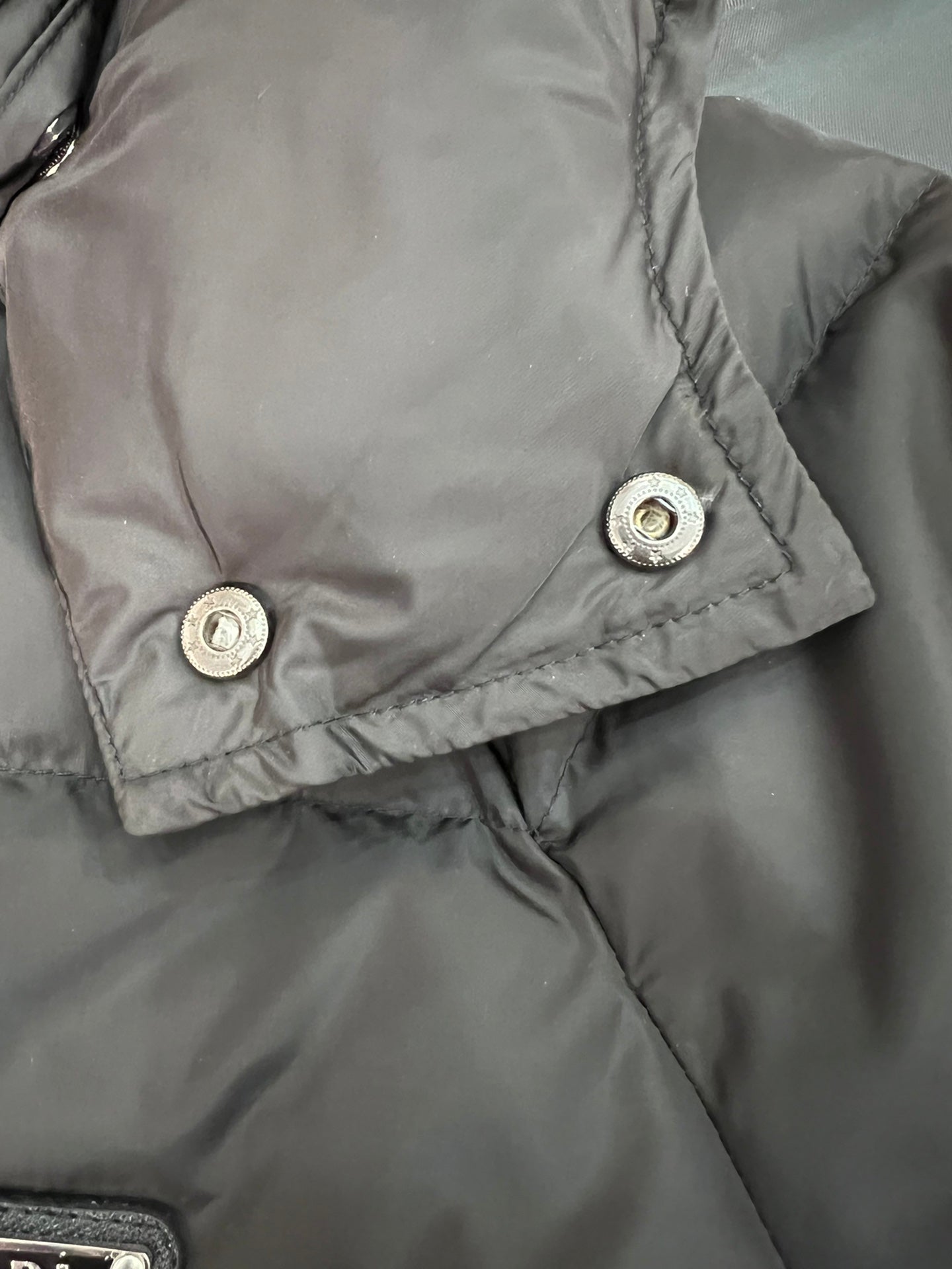 Gray long puffer jacket cuff with snap buttons and stitched trim.