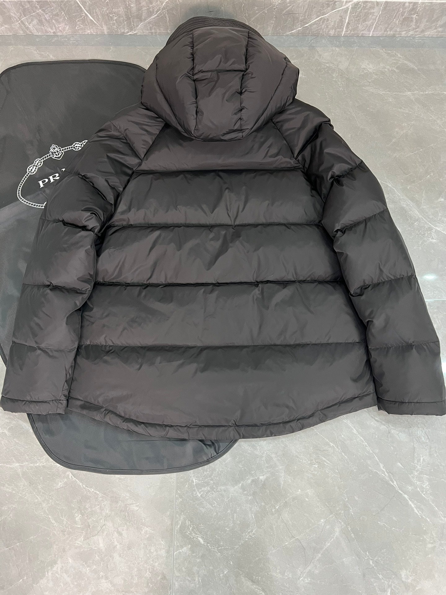 Black long puffer jacket with quilted back and attached hood.