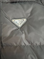 Logo patch on dark long puffer jacket chest area.