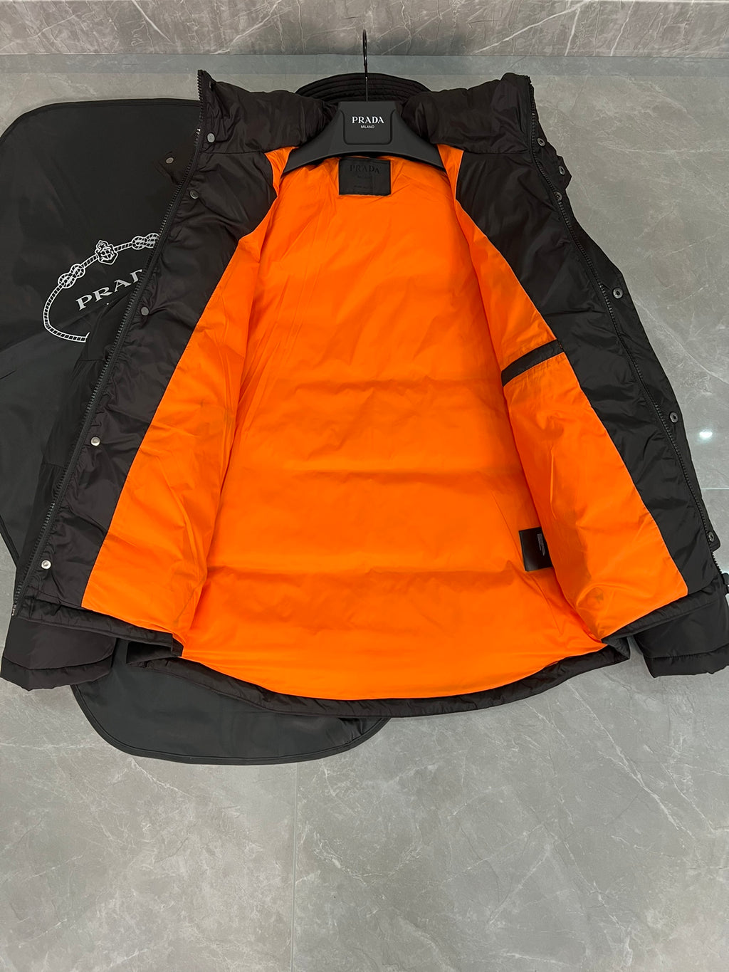 Black long puffer jacket with hood and orange inner lining panels.