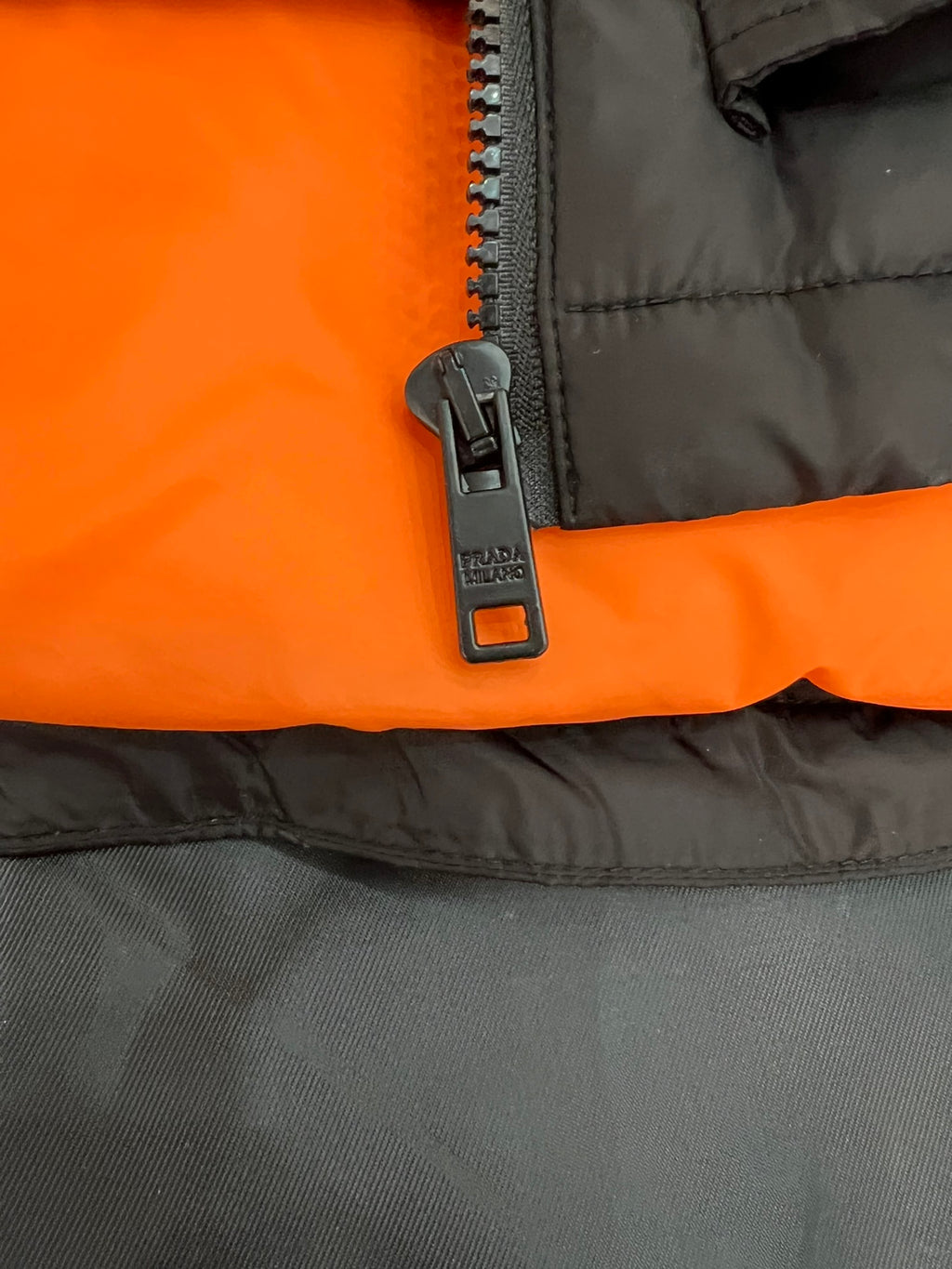 Zipper pull on orange lining of a black long puffer jacket.