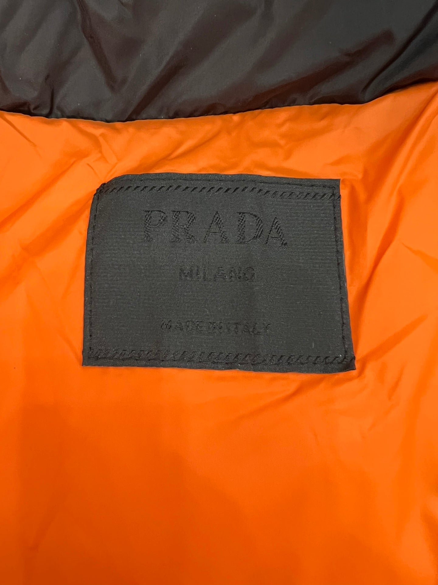 PRADA fabric label on orange lining of a long puffer jacket.