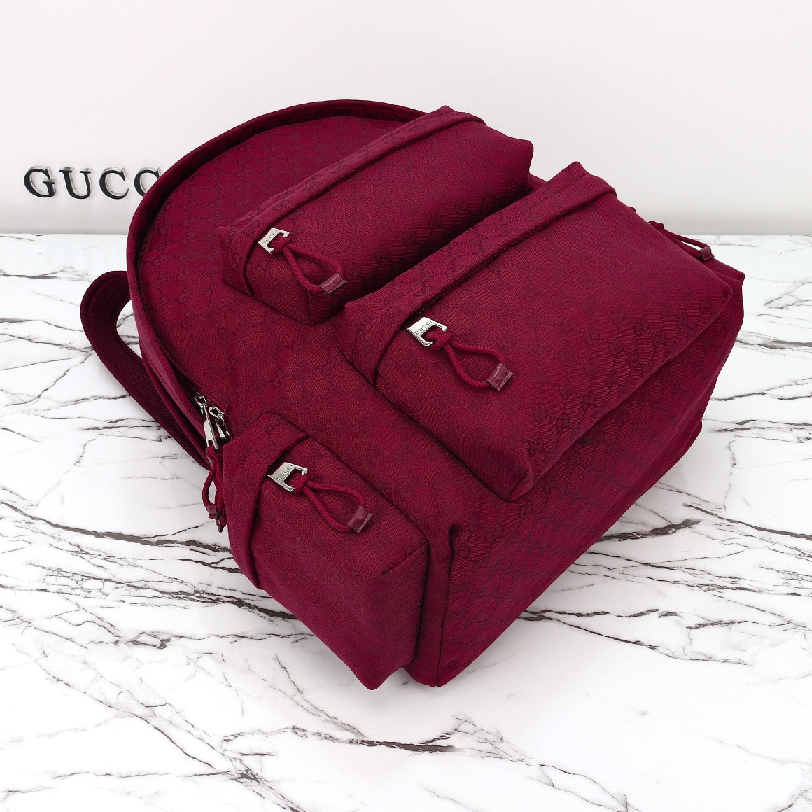Gucci burgundy monogram duffel bag with top handle, front flap, and multiple buckle straps