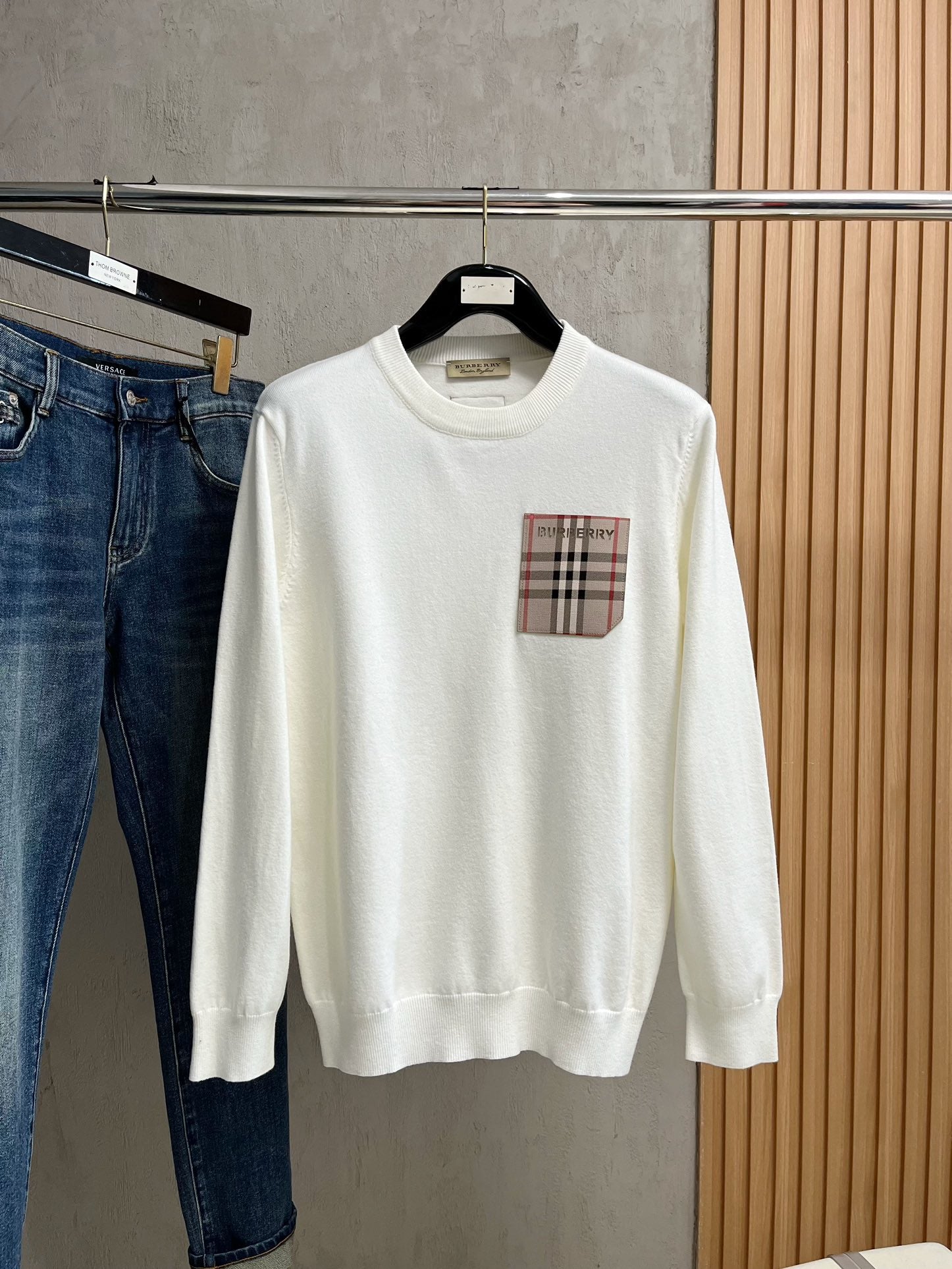 White crewneck sweatshirt with long sleeves and plaid logo chest patch