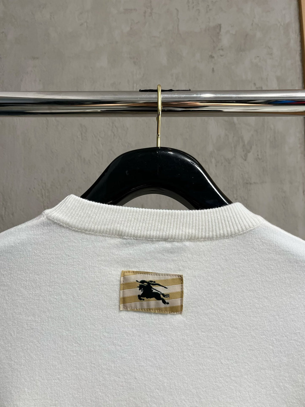 White sweatshirt back with small gold logo patch near the collar