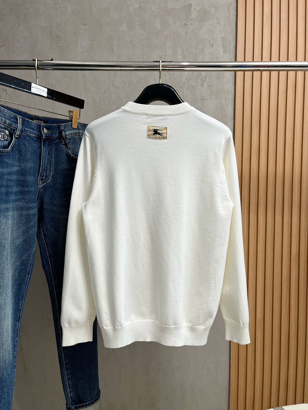White crewneck sweatshirt with long sleeves and gold logo patch on chest